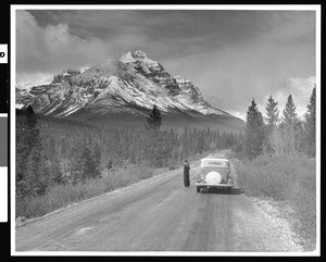 Woman standing with a car at the base of a mountain, Canada, ca.1930-1939