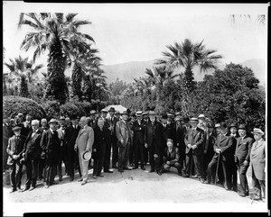 Members of the Sunset Club posing in front of a road lined with palm trees, ca.1900