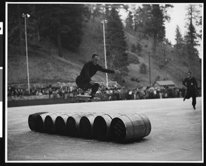 An ice skater performing jumps over a row of barrels at Big Pines mountain camp, ca.1930