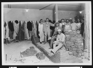 Portrait of group of masons near a brick wall in a room, ca.1930