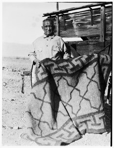 Old man holding up a blanket in front of a wagon