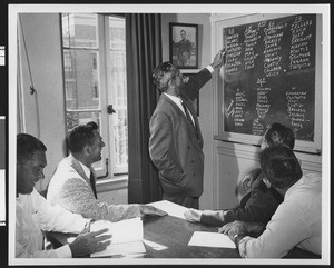 University of Southern California football coach Jess Hill pointing at a chalkboard with players' names on it, while four of his coaches look on, USC campus, 1951