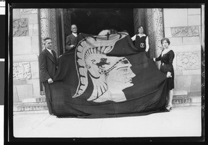 University of Southern California football coach Howard Jones and Bill Hunter holding the Trojan War Flag with two women, USC campus, 1928