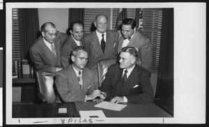 University of Southern California head football coach Jess Hill takes a pen from President Fagg as they sign Hill's new football contract, with Willett, Pappas, Hunter, and Bishop standing behind them, USC campus, January 1951