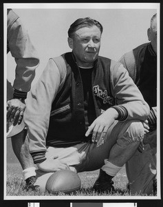 University of Southern California head football coach Jeff Cravath, full figure shot, on one knee, wearing a letter jacket, Bovard Field. 1949