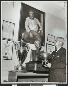 University of Southern California former football coach and athletic director Jess Hill looking up at portrait of Howard Jones and surrounded by football awards, USC campus, 1958