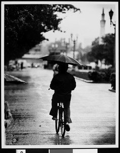 Student riding a bike in the rain, USC, 1977