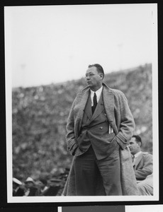 University of Southern California head football coach Jeff Cravath at the UCLA-USC game, hands in pockets, standing on sidelines, shot to knees, Los Angeles Coliseum, 1944