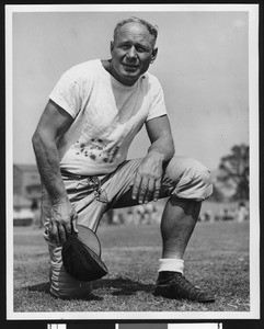 University of Southern California assistant football coach Roy "Bullet" Baker, on one knee, white tshirt, holding cap in hand, Bovard Field, 1946