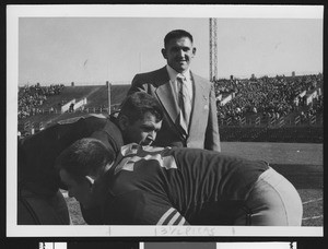 Navy football assistant coach Don Clark, wearing a suit, at pregame on Baltimore's Memorial Field with linebackers, 1950