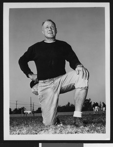 University of Southern California assistant football coach Roy "Bullet" Baker, on one knee, dark sweatshirt, holding cap in hand, Bovard Field, 1949