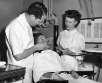 1960s - A local dentist gives a boy a check-up while the hygenist looks on