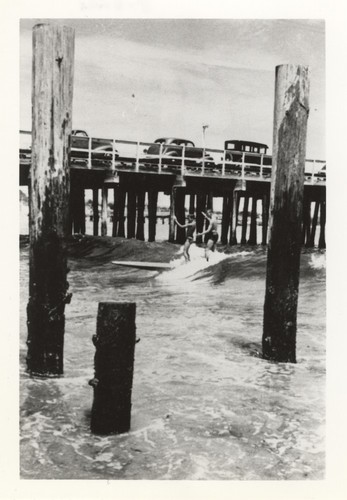 Rich Thompson and Harry Murray tandem surfing among pilings of the old 1922 wharf at Cowell Beach