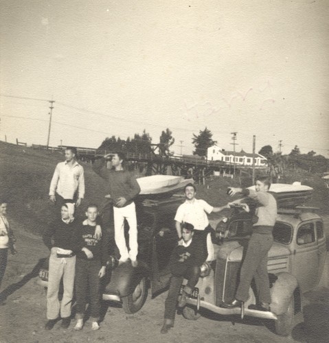 Dave "Buster" Steward, E. J. Oshier, Claude "Duke" Horan, Fred Hunt (front). Bob Sutter, P. B. "Smitty" Smith, Rich Thompson, Harry Mayo standing on automobiles at Cowell Beach in front of Dream Inn