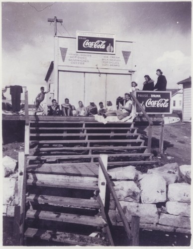 Unidentified surfer, Harry Mayo, Don Patterson, unidentified surfer, Fred Hunt, E. J. Oshier, two unidentified surfers, Nellie Patterson, Shirley Templeman at the clubhouse next to the board house Cowell Beach