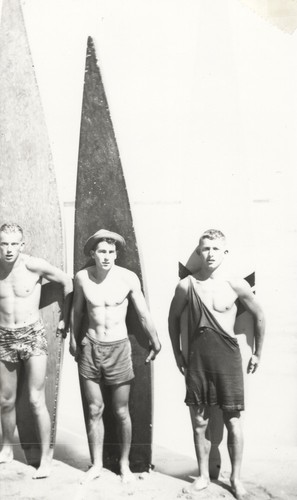 Rich Thompson, Harry Mayo, Bob Gillies in front of surfboards at Cowell Beach