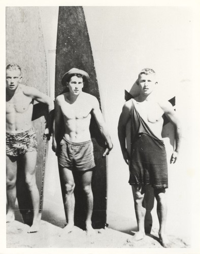 Rich Thompson, Harry Mayo, Bob Gillies in front of surfboards at Cowell Beach