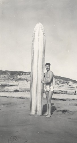 Alex Hokamp standing next to surfboard at Cowell Beach