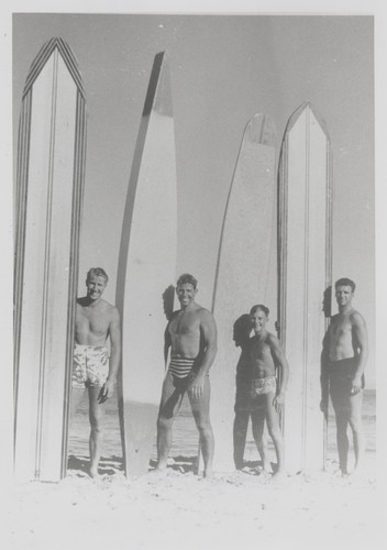 Fred Hunt, Don Patterson, Harry Murray, Alex Hokamp standing in front of surfboards at Cowell Beach