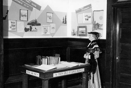 Ada Lou Hawes, wearing period costume, in front of a Santa Cruz history display