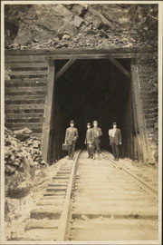 Four men standing on railroad tracks in front of a tunnel