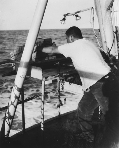 Significant knowledge of the structure of the earth beneath the sea is gathered from seismic studies. An explosive charge originates waves which travel through the sea floor and are picked up by a listening ship. Here Maxwell Silverman, engineer, pushes overboard a 200-point charge of TNT from the shooting table