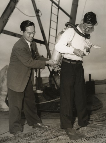 Japanese oceanographer Noriyuki Nasu (left) shown here assisting a Japanese aqualung demonstrator, Nasu later worked at the University of Tokyo's Ocean Research Institute and he also was a co-chief scientist during Leg 57 of the Deep Sea Drilling Project. "Aqualung" was the original name for the first open-circuit scuba diving equipment; it consists of a high pressure diving cylinder and a diving regulator that supplies the diver with breathing gas at ambient pressure, via a demand valve. 1953