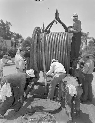 Field crews installing country's largest capacity high voltage underground electric cable. Reels hold 710-ft of cable, standard span between manholes