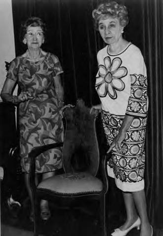 Two women standing next to a chair in the Avila Adobe