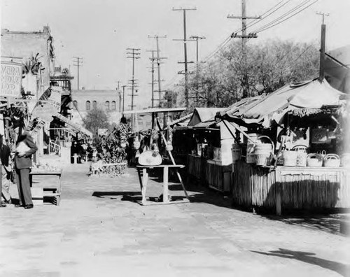 Shot of Olvera Street lined with booths on the right and on the left, the Olvera Candle Shop and La Golondrina and a "Portraits and Caricatures" booth