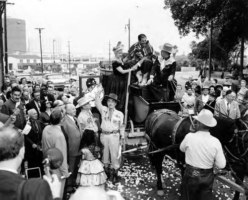 Crowd surrounding a stage coach with Sheriff Pitchess sitting on top in front of the Simpson building