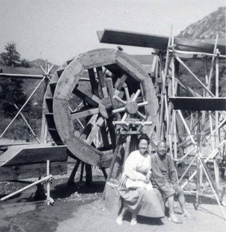 A woman and a man seated in front of a waterwheel. On the back of the photo it reads "Slosson Jong- Lost Horizon 1972"