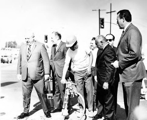 Sam Yorty, Lindsay and men standing around a worker at the Sunset Boulevard closing