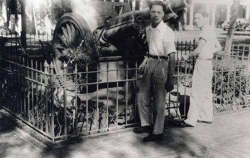 Two men standing in front of a gated artillery