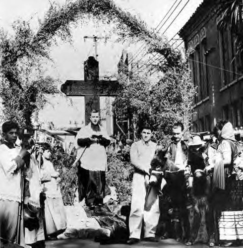 Priest is reading scriptures from the bible and all are standing in front of the cross on Olvera Street