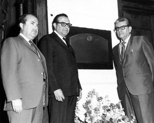 Three men standing by Christine Sterling plaque