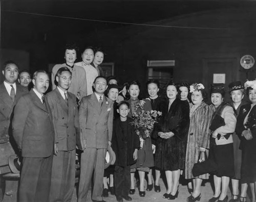 Formal photograph of Yee Good Gal in a China doll haircut and Cheong-Sam surrounded by her four children: Stanley, Robert, Lillian and Peter. The photo was taken in a photographer's studio in Canton, China with a European style villa backdrop in 1930