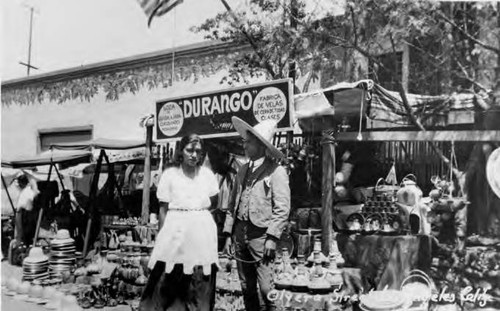 Olvera Street in front of where El Paseo is now. Pictured is the Durango outside shop with merchandise spread out on street and Mr. Gonzalez with unidentified woman in front of merchandise