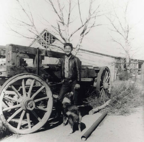 Man in a leather jacket, gingham shirt and jeans standing in front of a pull cart