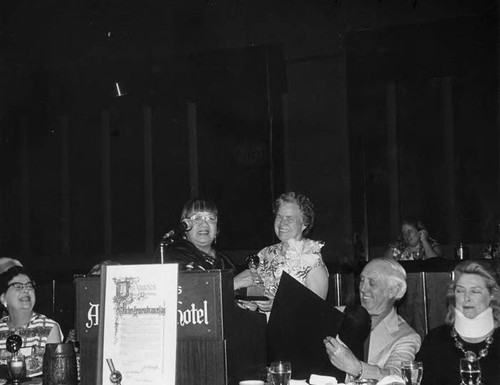 Lily Lum Chan, the secretary of Teacher's Remembrance Day Board, presented Mary Montgomery (honoree) an award at the Coconut Grove in the Ambassador Hotel