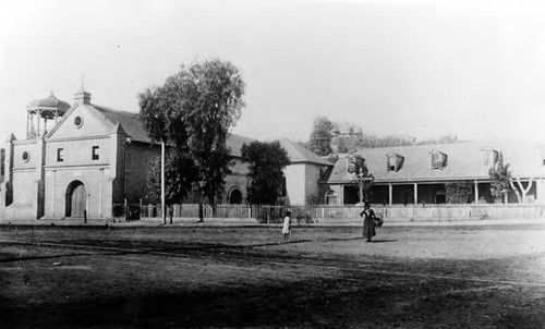 Plaza Church with gothic bell tower and rectory shown with railroad tracks in front