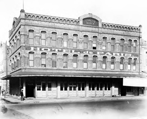 Photograph of Jennette Block on Los Angeles Street, which the Hotel de Paris occupied. There is a noodle restaurant on the left corner of the building where the Chinese man is standing