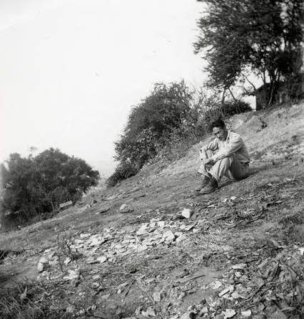 A man sitting on a hillside. Text on the back reads "Our lot the week before" (Spencer Chan Family)