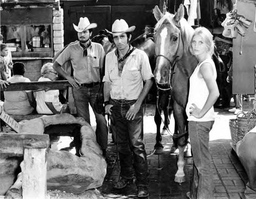 Two men and one woman with horses at a water trough