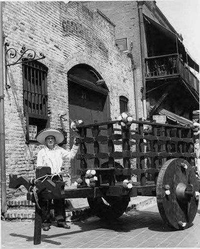 Man with cart on Olvera Street with Sepulveda House in the background