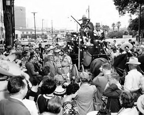 Crowd surrounding a stage coach that Sheriff Pitchess is sitting on top of in front of the Simpson building