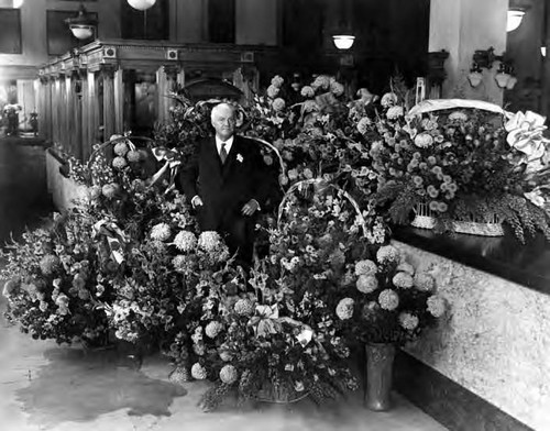 Harry Chandler surrounded by baskets of flowers