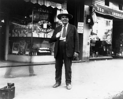 Man, possibly the owner, standing in front of Botica Ruiz, near the plaza