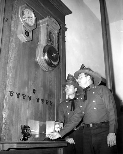 Two firemen next to Firehouse fire bell