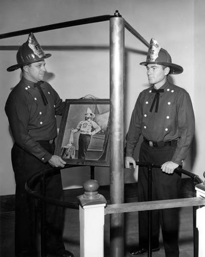 Two firemen with picture standing by pole